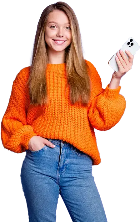 A girl wearing a long sleeve sweater and jeans is smiling and holding an iphone in her left hand.